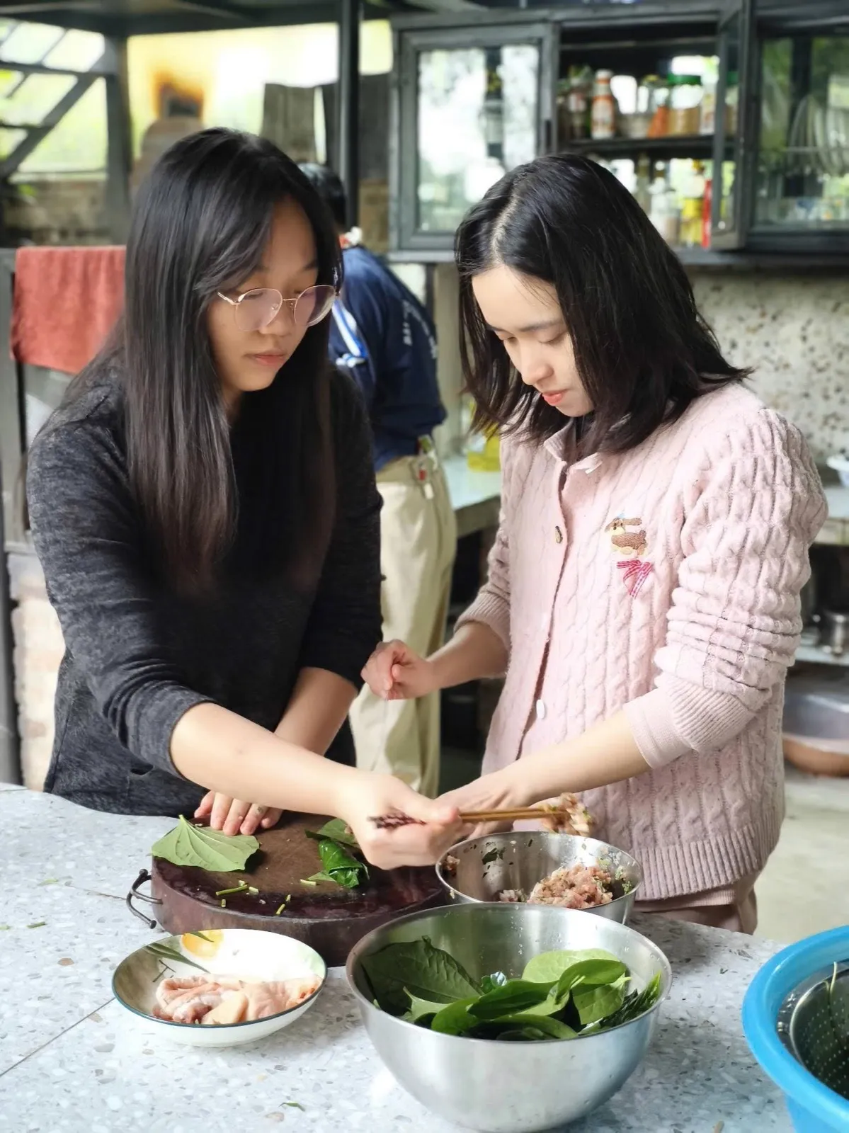 Hai đôi tay cùng cuốn lá lốt bên thớt gỗ trong gian bếp ở Làng Hạnh Phúc 5M