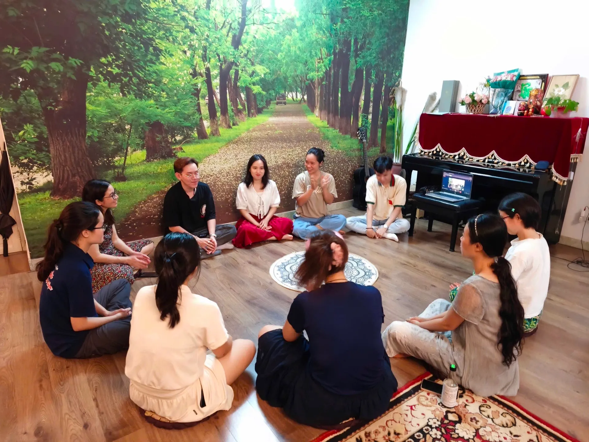 Một nhóm người ngồi thành vòng tròn trên sàn nhà, cùng lắng nghe một người đang chia sẻ